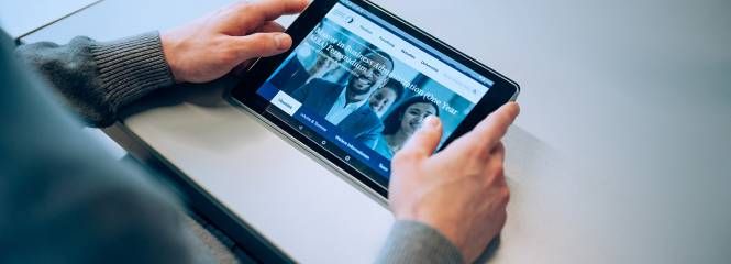 Person sits on a table and takes a closer look at a study program on a tablet
